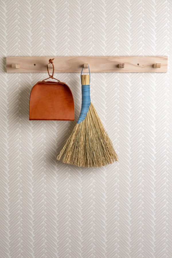 Broom and dustpan hanging on a wooden rack against a textured wall.