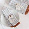Blue and white checkered napkins with brown trim on a marble surface.