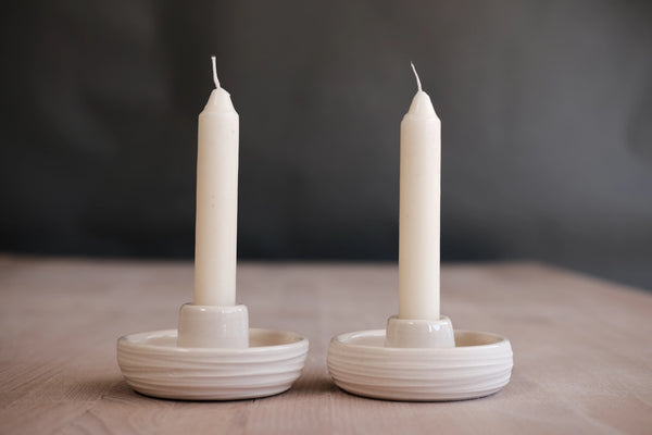 Two white candles in ceramic holders on a wooden surface with a dark background