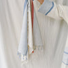 Person wearing a white shirt with a striped towel draped over their shoulder against a plain background
