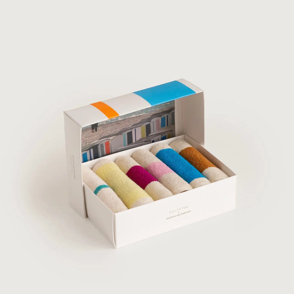 A white gift box containing six rolled pairs of multicolored towels, shown open on a light gray background. The towels are in pastel and bright shades of yellow, pink, blue, orange, and cream.