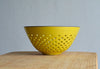 Yellow colander/berry bowl on a wooden surface with a gray background