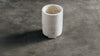 A small cylindrical white marble wine cooler made of natural marble, standing on a textured dark gray surface.