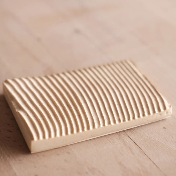 Rectangular ceramics soap dish with grooved surface on a wooden surface