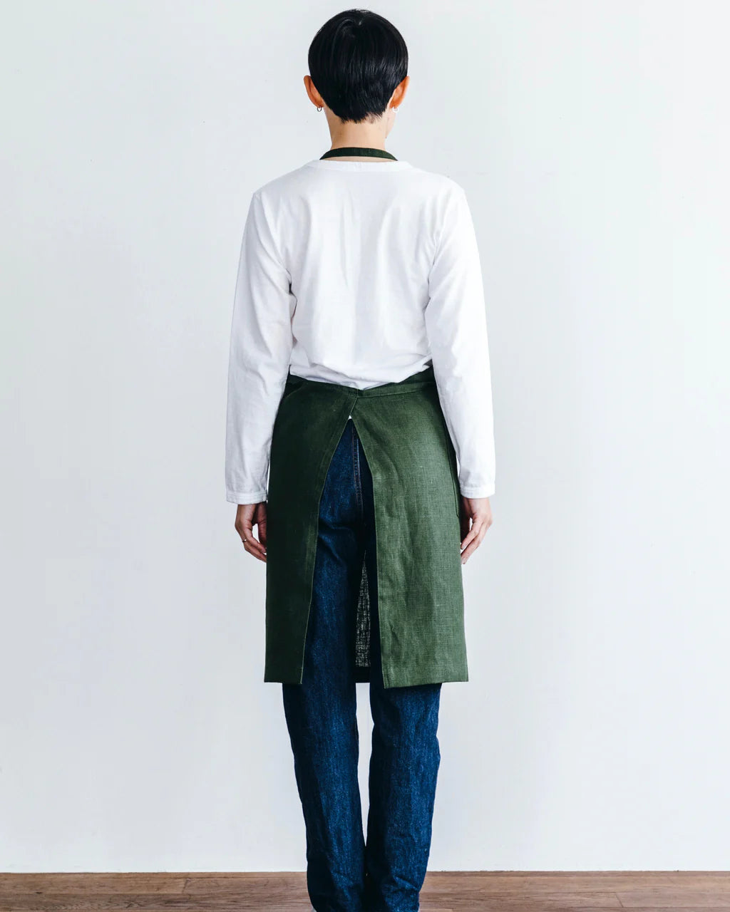 Person wearing a white shirt and green apron against a plain background
