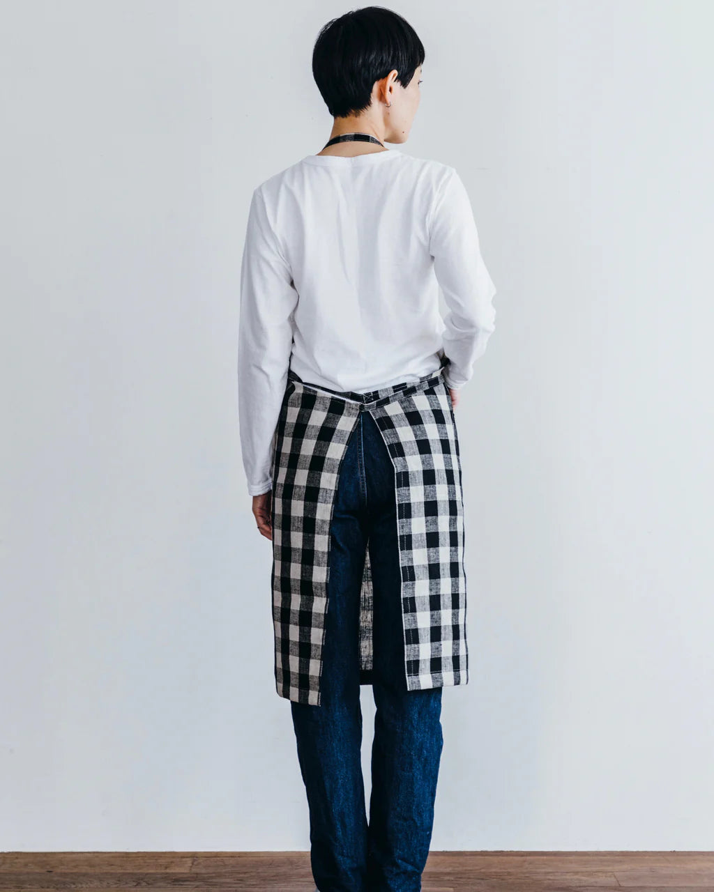 Person wearing a white shirt and plaid apron against a plain background