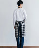 Person wearing a white shirt and plaid apron against a plain background