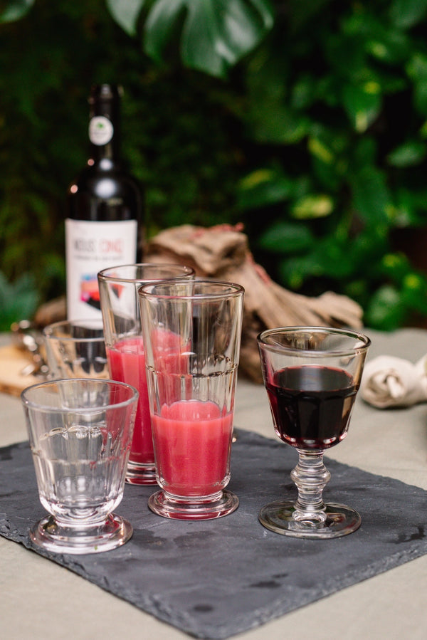 Set of glasses with different beverages on a slate surface with a bottle in the background.