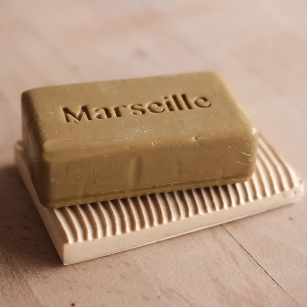 Bar of Marseille soap on a ceramic soap dish with 'Marseille' branding.