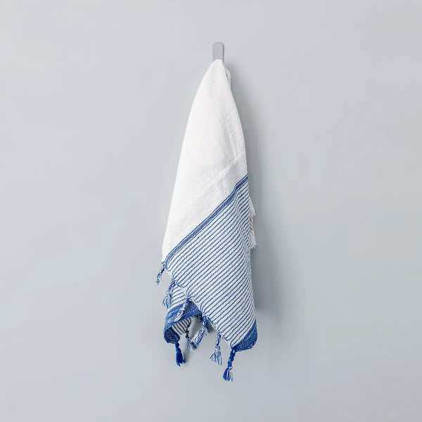White towel with blue stripes and tassels hanging on a gray wall.