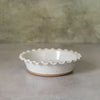 A small round ceramic pie dish with a scalloped rim and a speckled off-white glaze, set on a gray surface against a textured gray background.