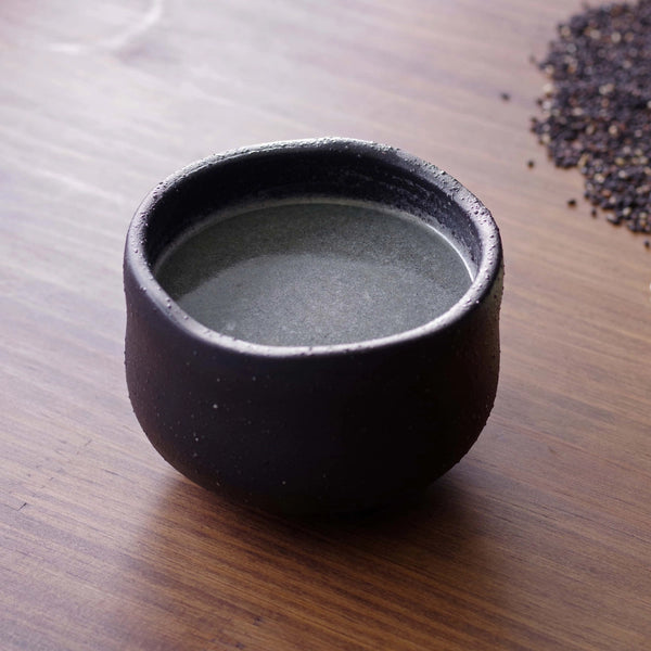 Black ceramic cup with a small amount of liquid on a wooden surface