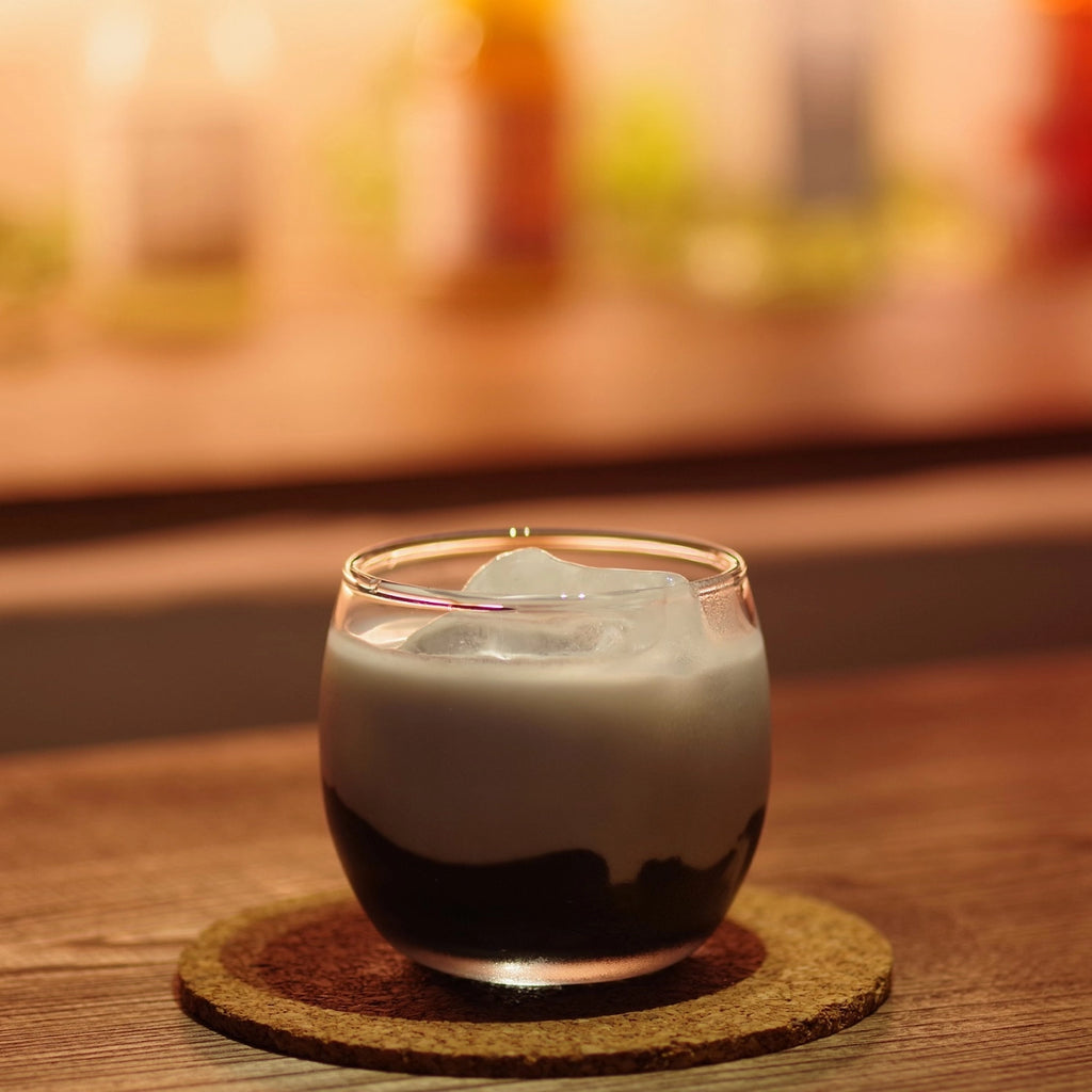 Glass of layered drink on a cork coaster with a blurred background