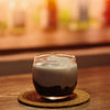 Glass of layered drink on a cork coaster with a blurred background