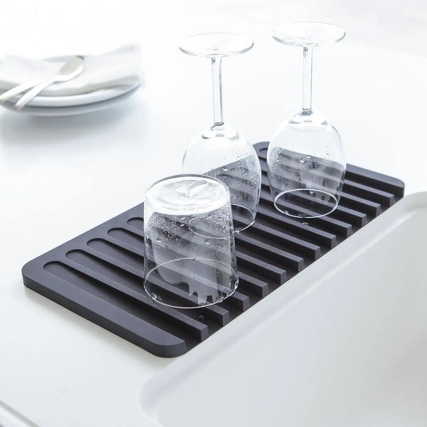 A black silicone kitchen drying rack placed in a white sink, holding three clear drinking glasses.