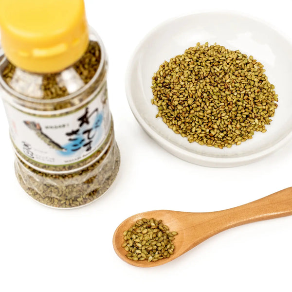 Spice jar, wooden spoon with spice, and plate of sesame seeds on a white background