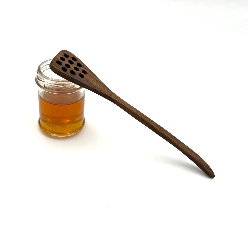 Wooden honey dipper next to a jar of honey on a white background