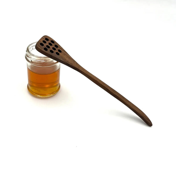 Wooden honey dipper next to a jar of honey on a white background