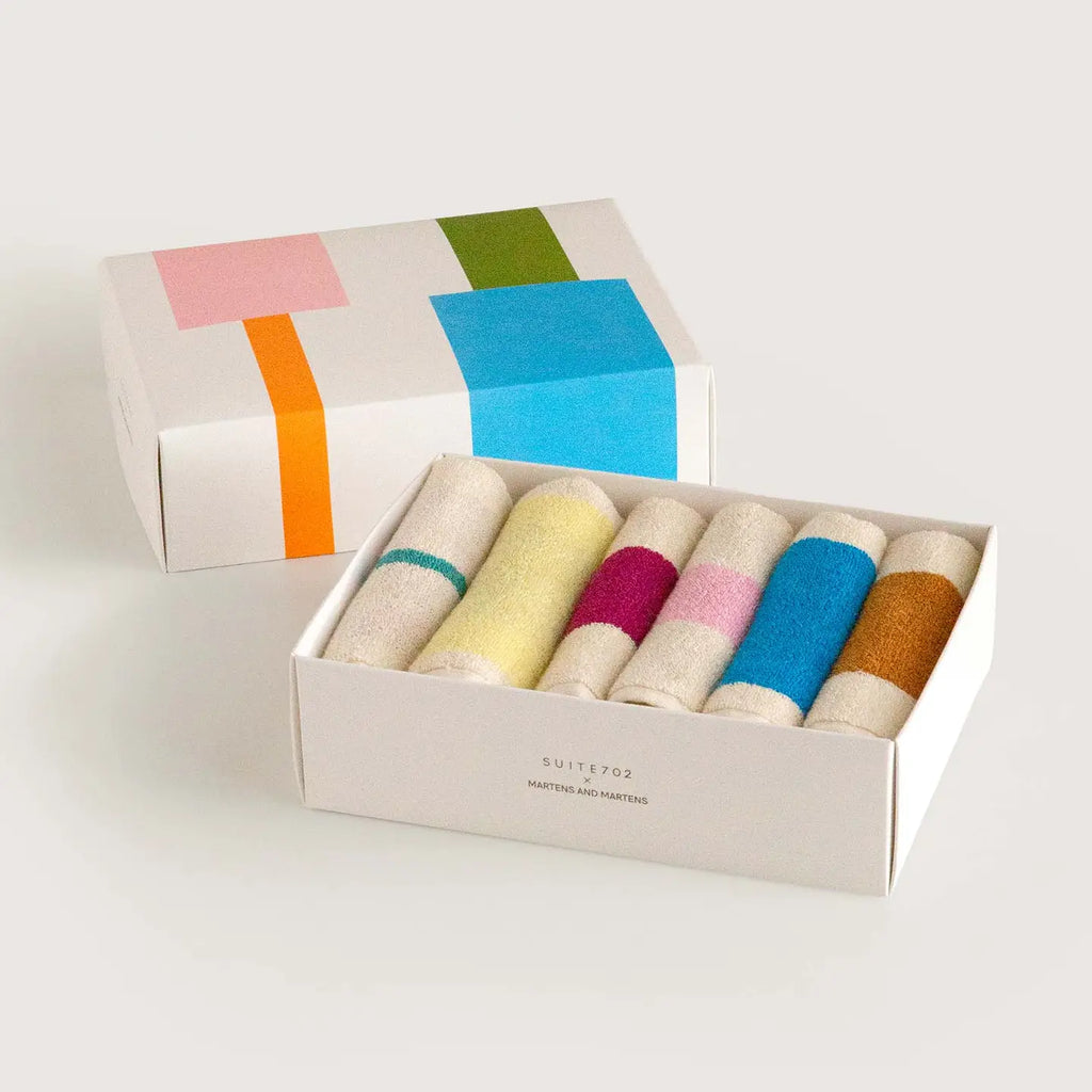 A boxed set of six rolled hand towels in assorted soft colors, shown open with the matching gift box behind it on a clean light gray background.