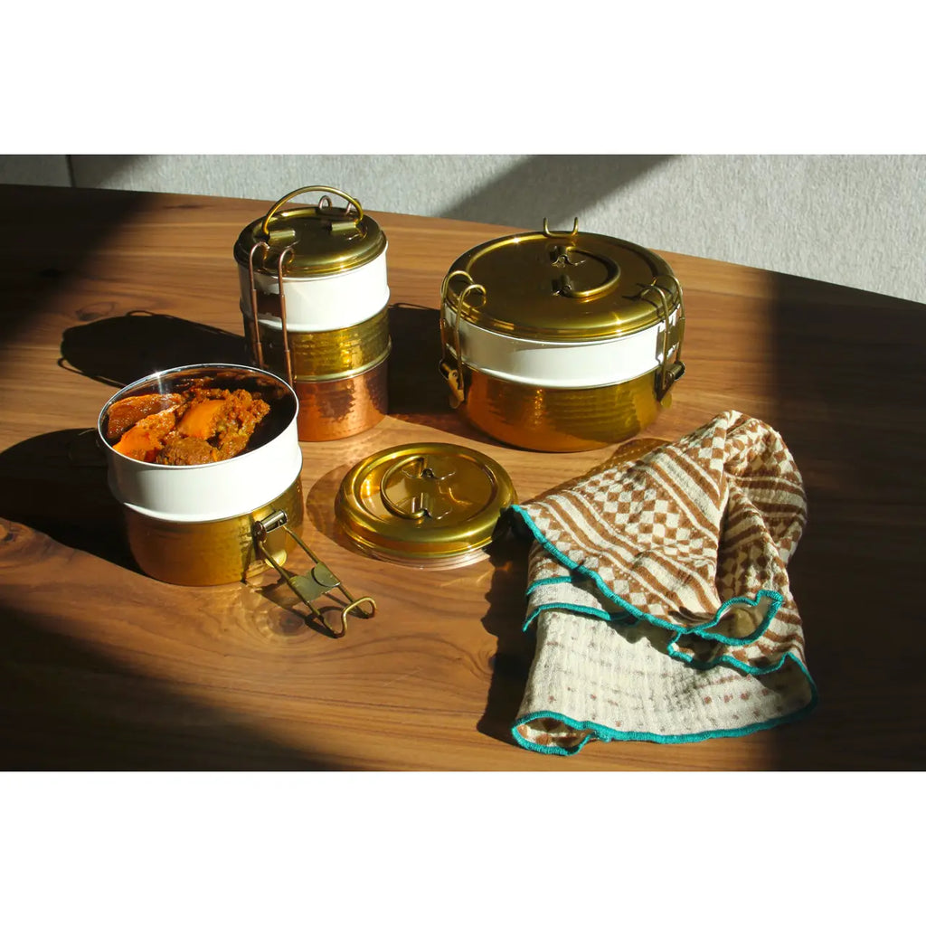 Set of metal food containers with gold lids on a wooden surface.