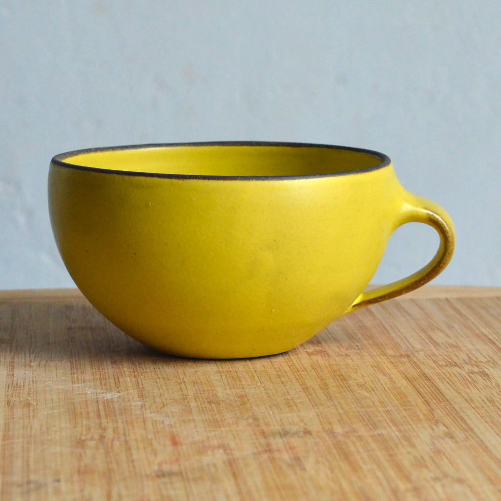 Yellow mug with black rim on a wooden surface and light blue background
