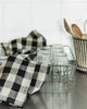 Black and white checkered towel on a kitchen counter with glasses and utensils.