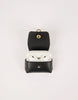Black leather case with gold accents containing white earbuds on a light gray background