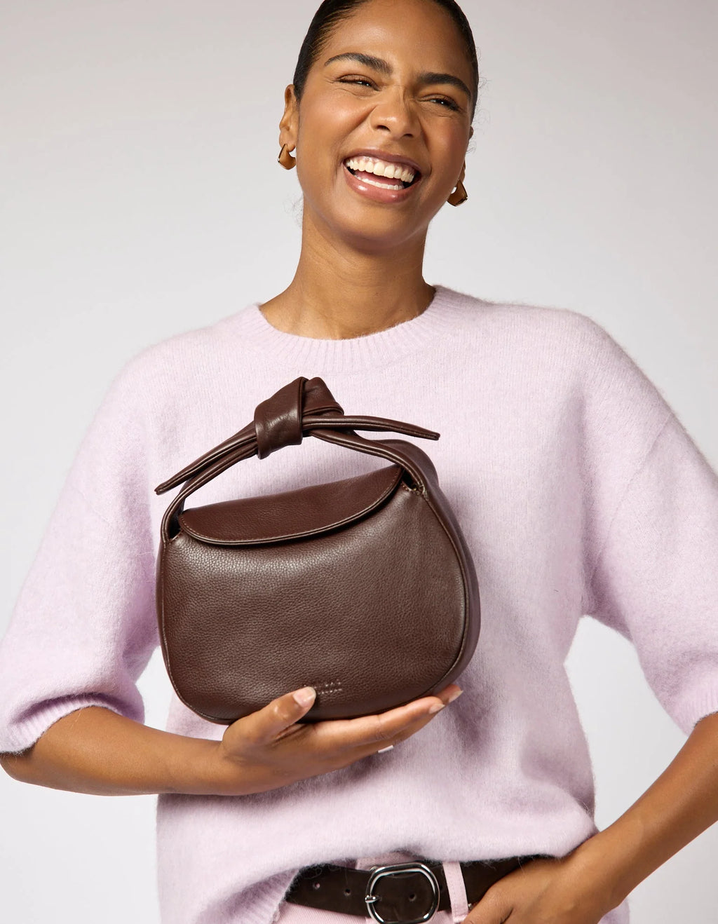 Woman holding a brown leather handbag against a plain background