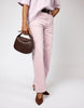 Person wearing light pink pants and holding a brown handbag on a white background