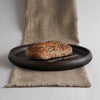 Loaf of bread on a black plate with a knife on a textured fabric surface