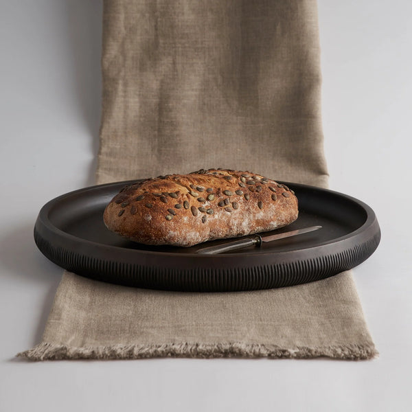 Loaf of bread on a black plate with a knife on a textured fabric surface