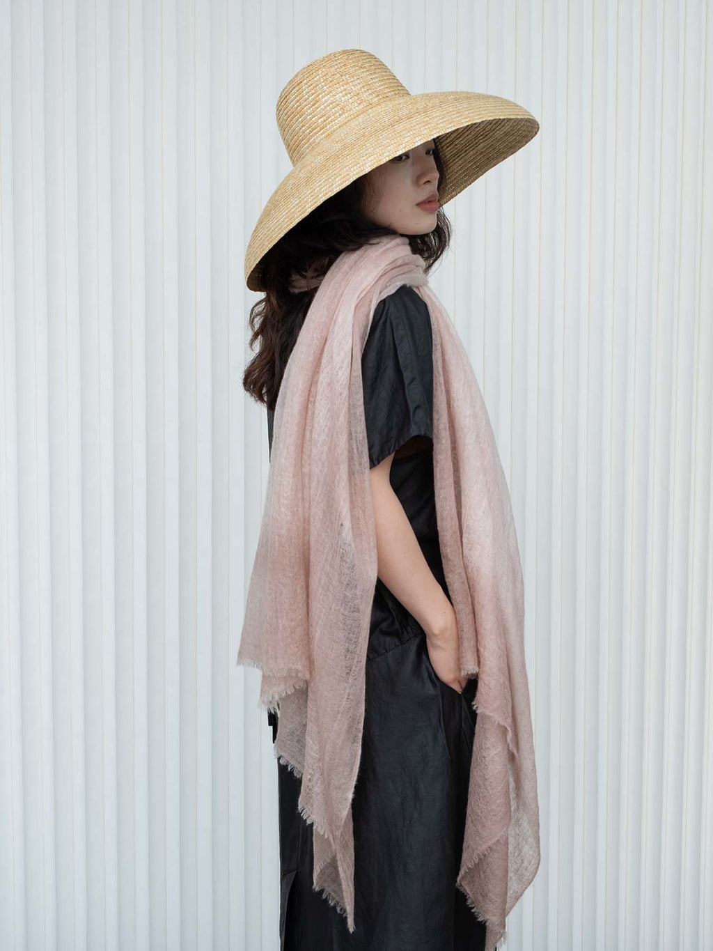 Woman wearing a wide-brimmed hat and a light pink scarf against a white background