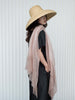 Woman wearing a wide-brimmed hat and a light pink scarf against a white background