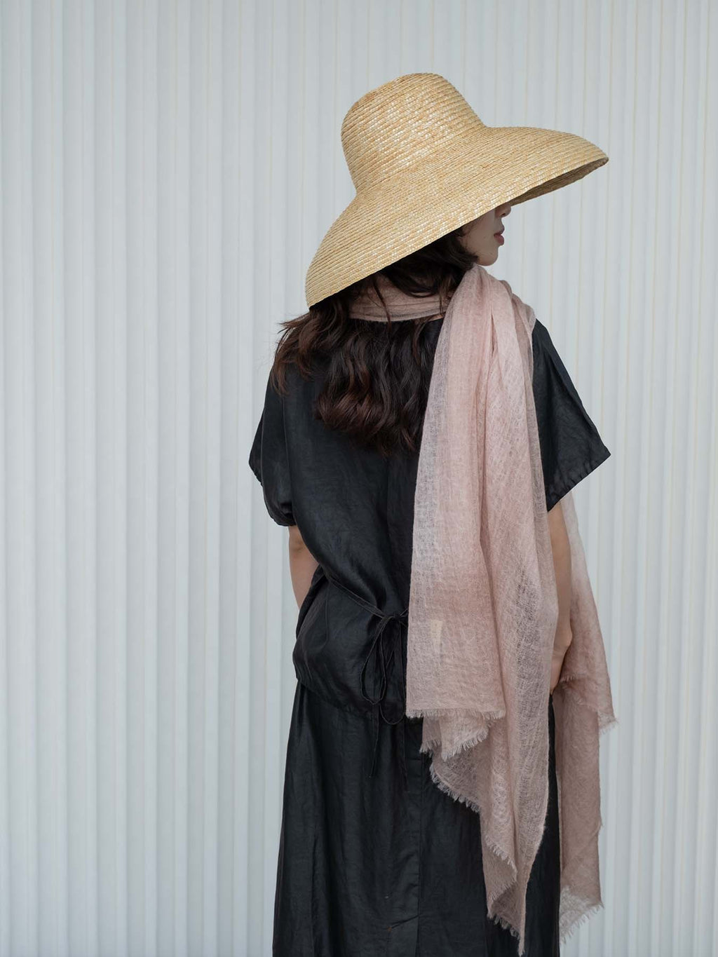 Person wearing a wide-brimmed hat and a light pink scarf against a white background