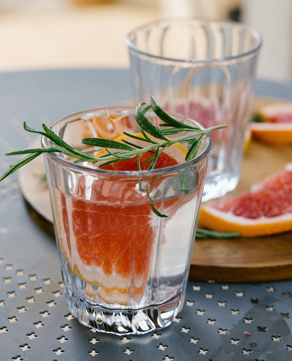 Clear glass with grapefruit and rosemary on a metal surface