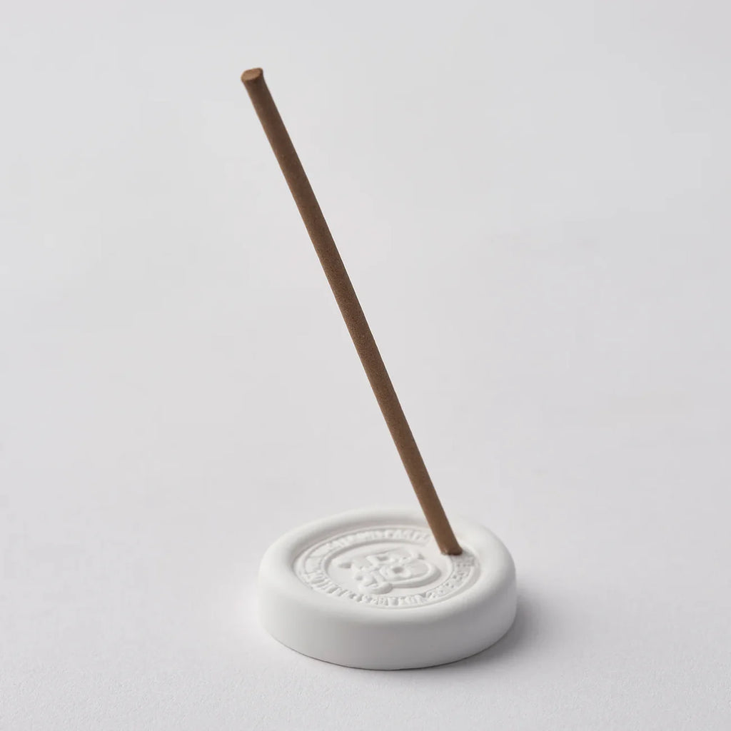 White incense holder with a single incense stick on a light gray background