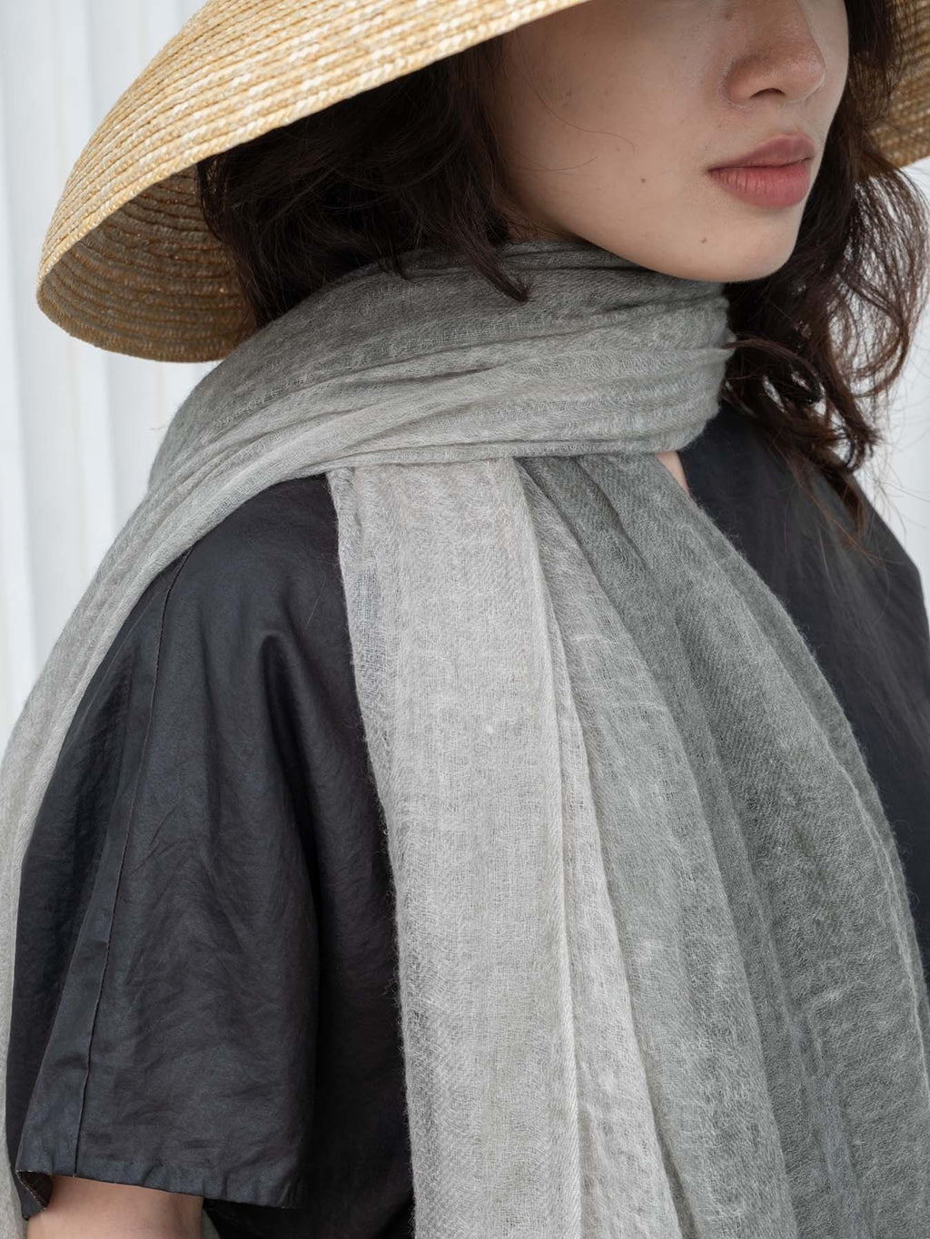 Person wearing a wide-brimmed hat and gray scarf against a white background