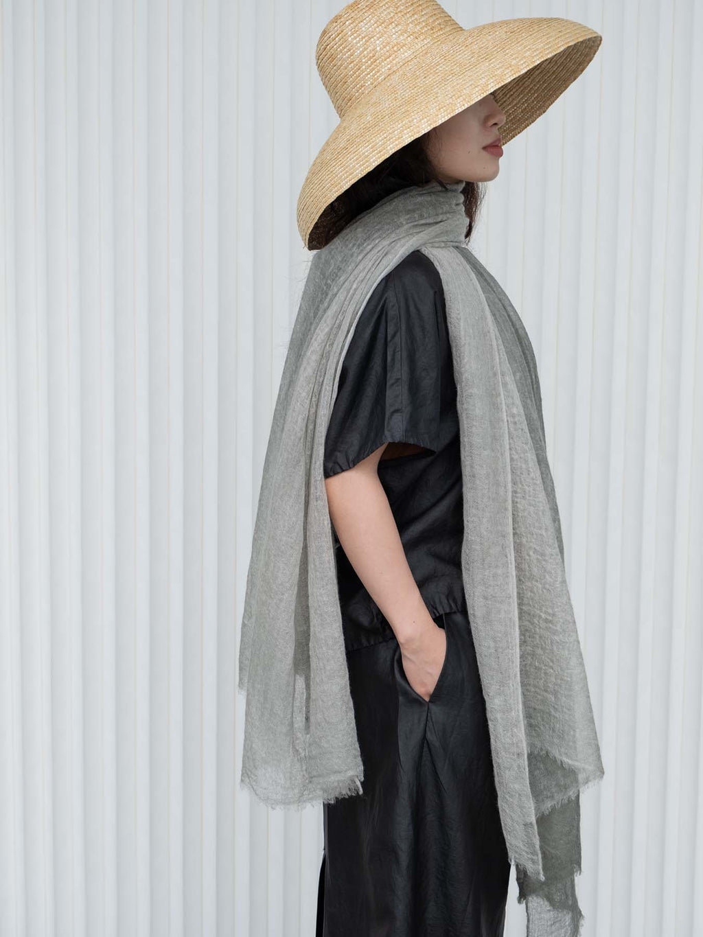 Person wearing a straw hat and gray scarf against a white background