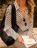 Person wearing a black and white striped outfit holding a book with a black tote on their shoulder