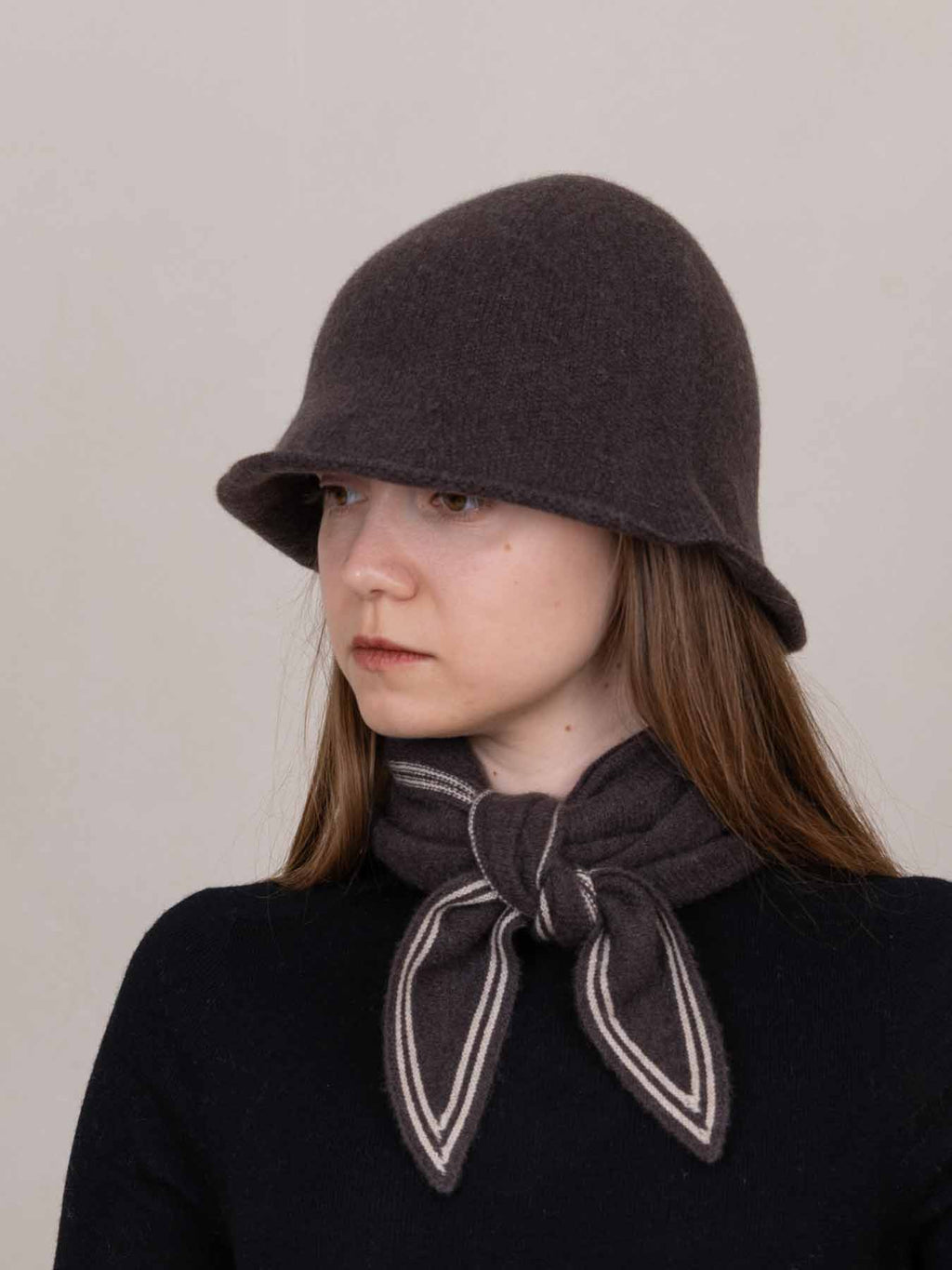 Woman wearing a dark brown cloche hat and matching scarf against a plain background