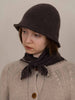 Person wearing a dark knitted hat and scarf with a beige sweater against a plain background
