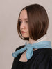 Woman wearing a light blue scarf around her neck against a plain background