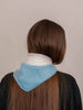 A person shown from the back wearing a light blue bandana-style neck scarf over a white inner collar, with long brown hair and a black top against a plain beige background.