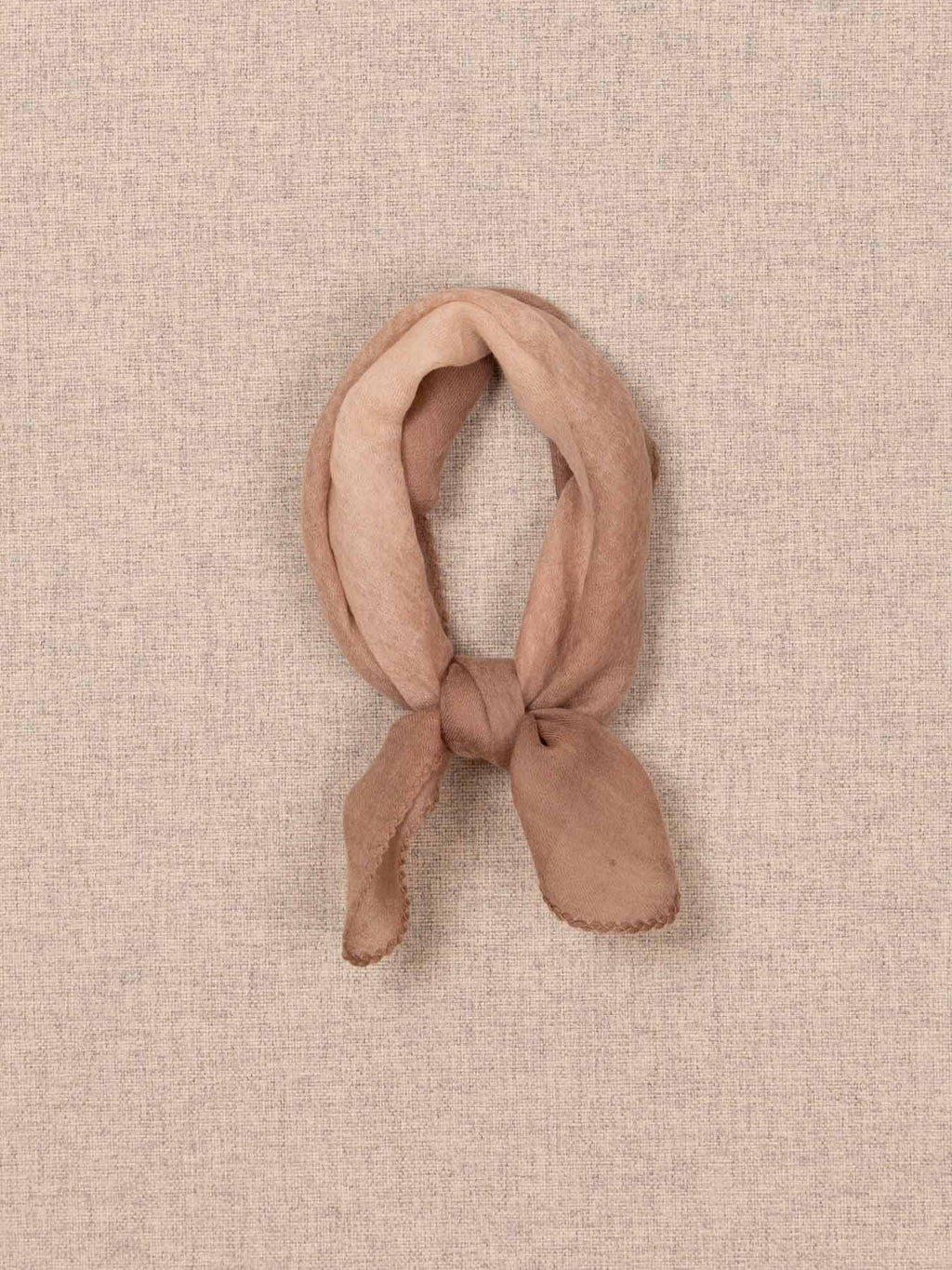 Pink knotted scarf on a beige textured background.