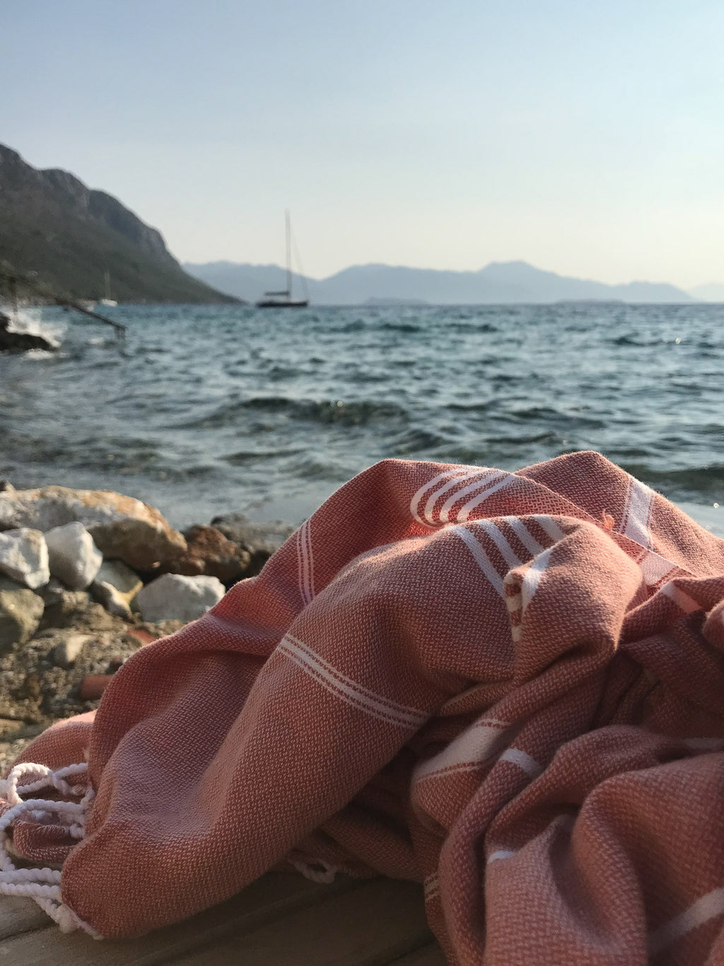 Pink towel with white stripes on a wooden surface by the sea