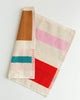 A folded cotton towel with a striped pattern in cream, pink, red, teal, and brown, displayed on a clean white background.