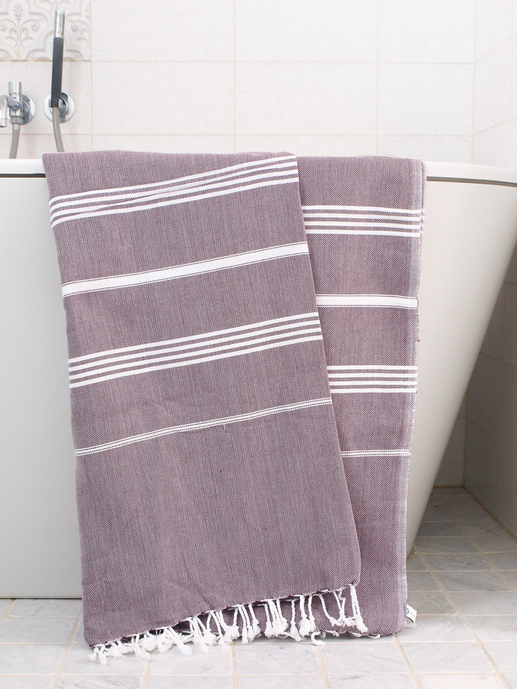 Purple towel with white stripes draped over a bathtub.