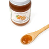 Jar of organic Amanatsu & Lemon spread with a wooden spoon containing some of the spread on a white background.
