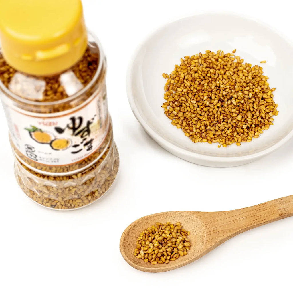 Bottle of YUZU SESAME seeds with a wooden spoon and plate of seeds on a white background