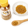 Bottle of YUZU SESAME seeds with a wooden spoon and plate of seeds on a white background